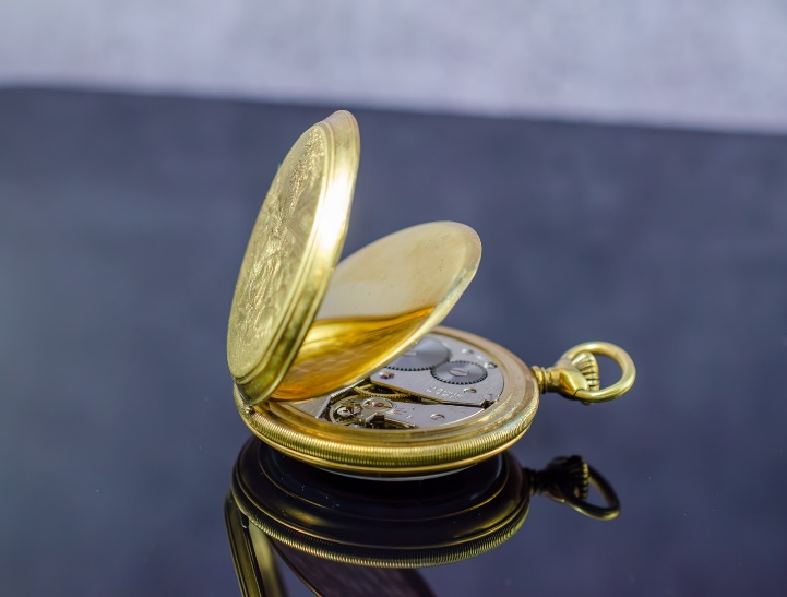 A gold pocket watch on a black surface Description automatically generated