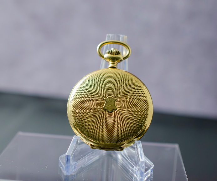 A gold pocket watch on a clear stand Description automatically generated