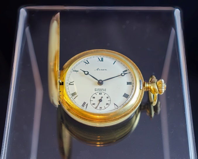 A gold pocket watch on a glass surface Description automatically generated with medium confidence