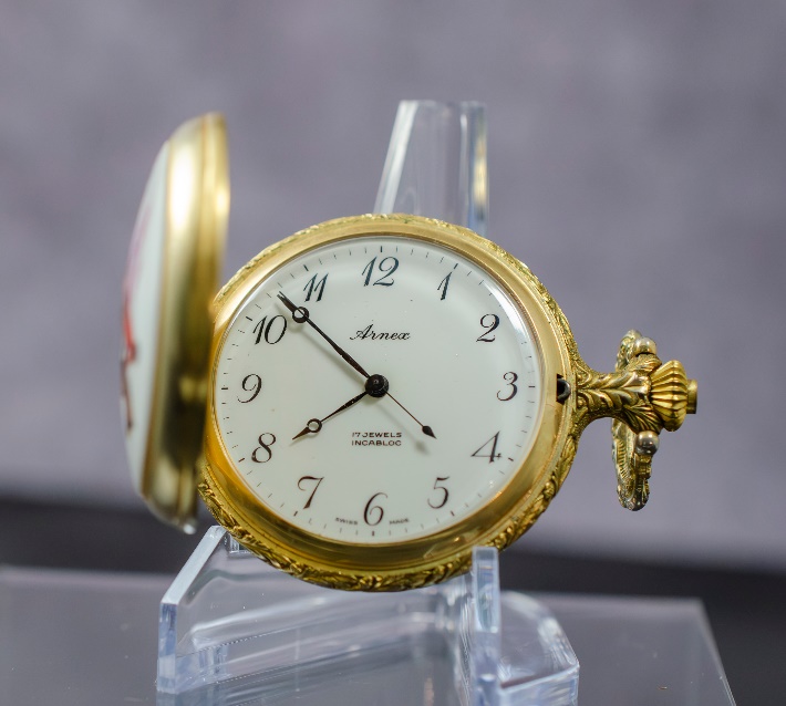 A gold pocket watch on a stand Description automatically generated