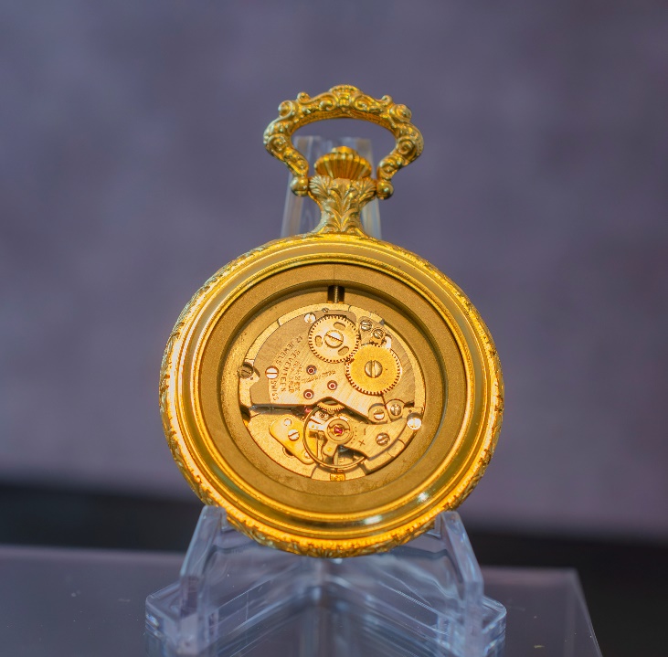 A gold pocket watch on a stand Description automatically generated