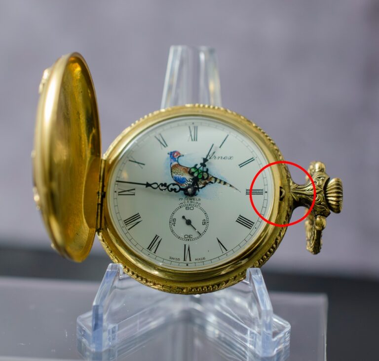 A gold pocket watch with a bird on it Description automatically generated