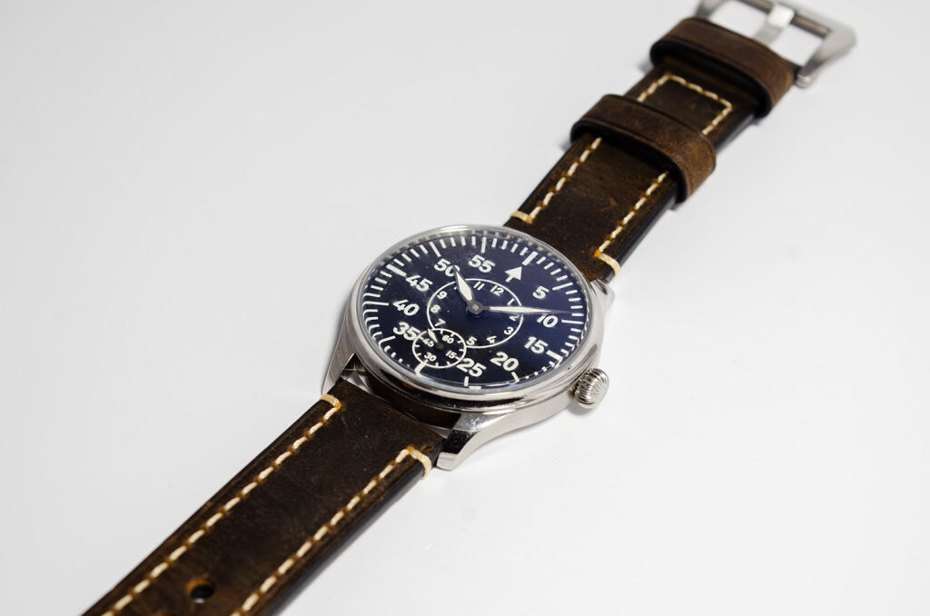 Beobachtungsuhr worn on wrist with brown leather strap, black dial, and white numerals shown in natural light