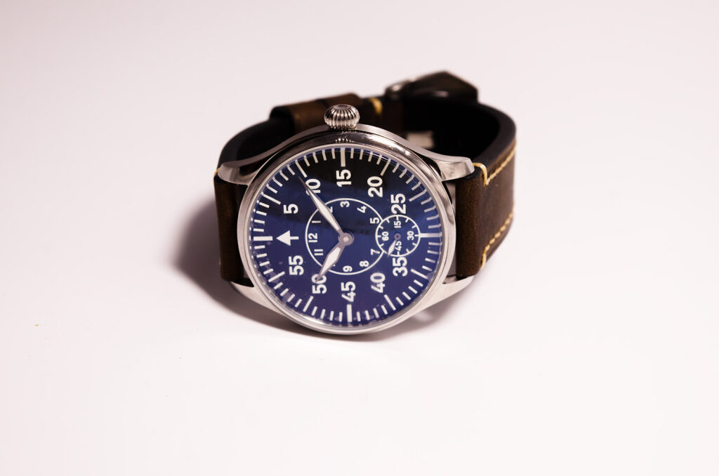 Frontal image of a Beobachtungsuhr chronograph featuring blue dial, three subdials, white numerals, sword-style silver hands, and brown leather strap
